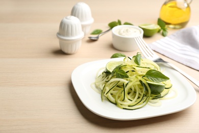 Tasty zucchini pasta with basil and lime served on wooden table. Space for text