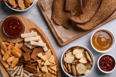 Photo of Different crispy rusks and dip sauces on light marble table, flat lay