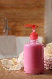 Dispenser of liquid soap and orchid flower on wooden table in bathroom