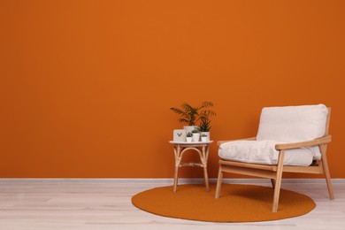 Image of Stylish room interior with armchair and green plants near orange wall, space for text