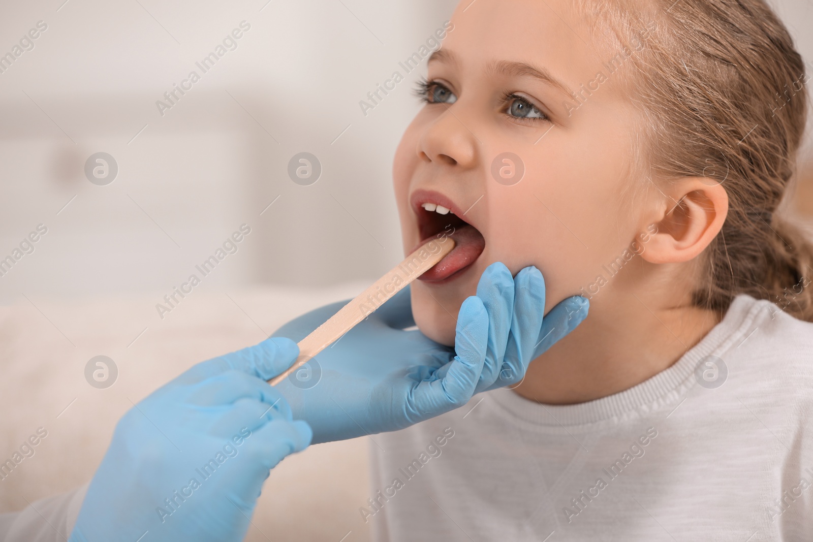 Photo of Doctor examining girl`s oral cavity with tongue depressor on blurred background, closeup. Space for text