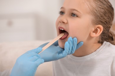 Photo of Doctor examining girl`s oral cavity with tongue depressor on blurred background, closeup. Space for text