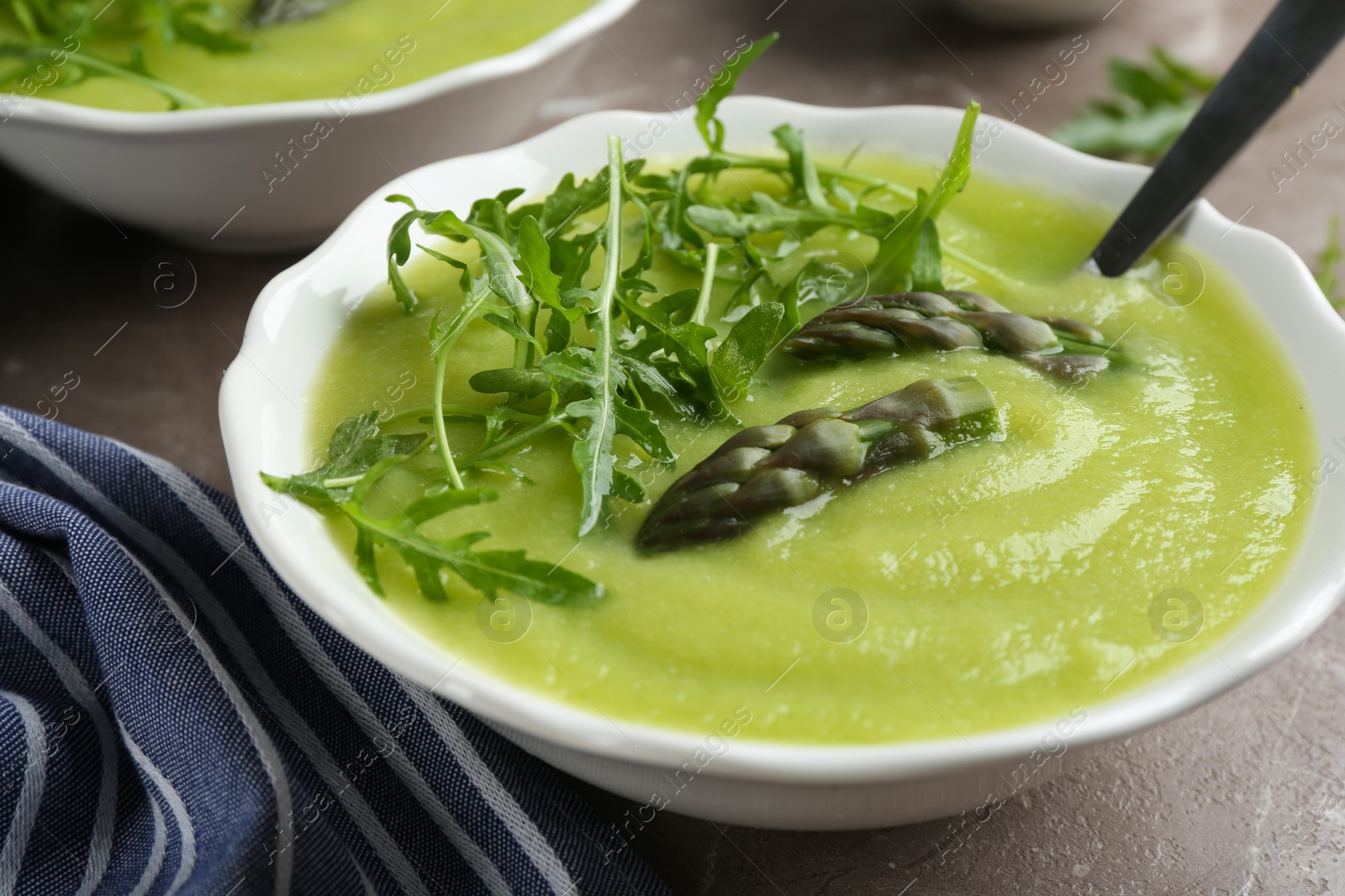 Photo of Delicious asparagus soup served on grey marble table, closeup