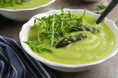 Photo of Delicious asparagus soup served on grey marble table, closeup