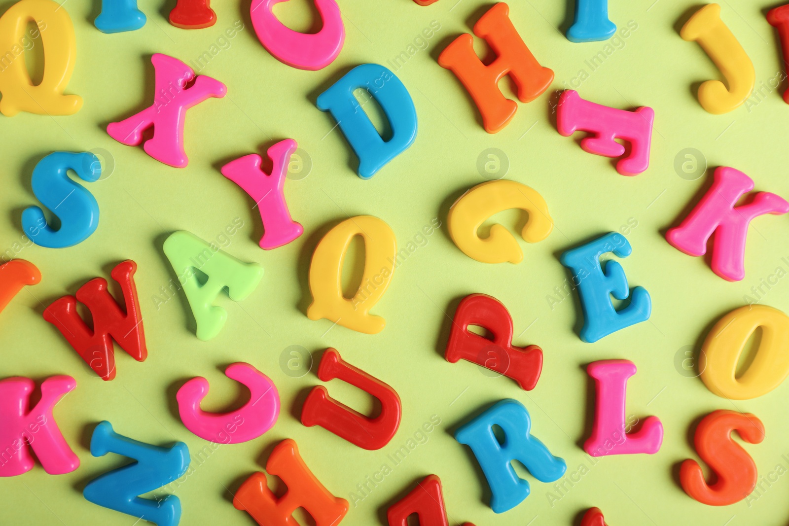 Photo of Many colorful magnetic letters on light green background, flat lay