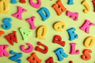Photo of Many colorful magnetic letters on light green background, flat lay