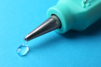 Melted glue dripping out of hot gun nozzle on light blue background, closeup
