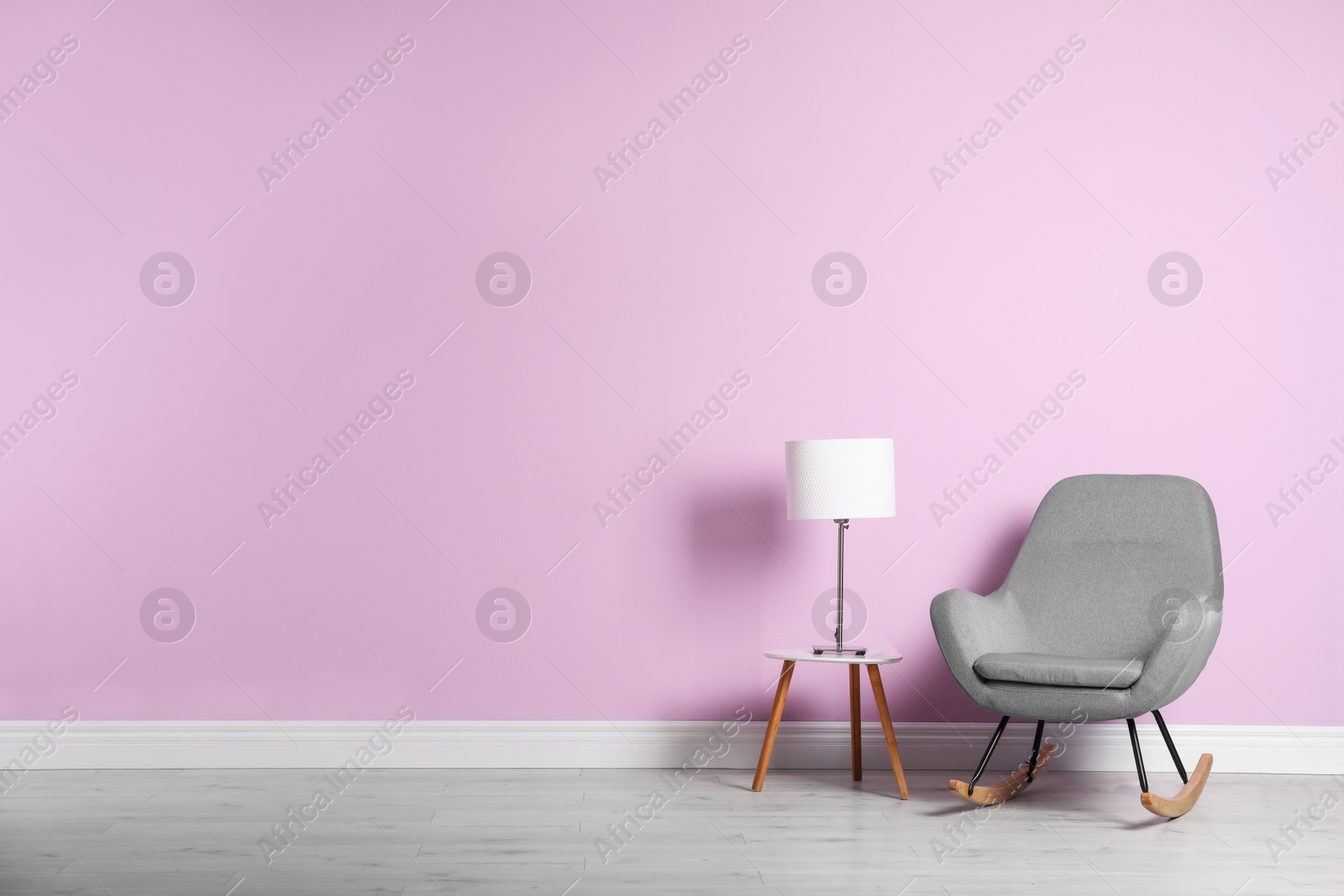 Photo of Rocking chair and lamp on table near color wall with space for text. Interior element