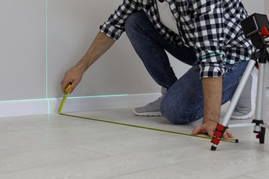 Photo of Man using cross line laser level and tape for accurate measurement on floor, closeup