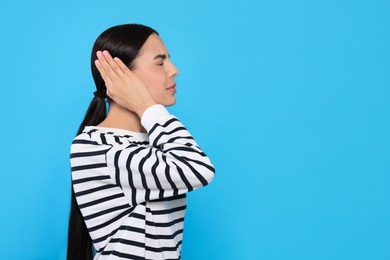 Young woman suffering from ear pain on light blue background. Space for text