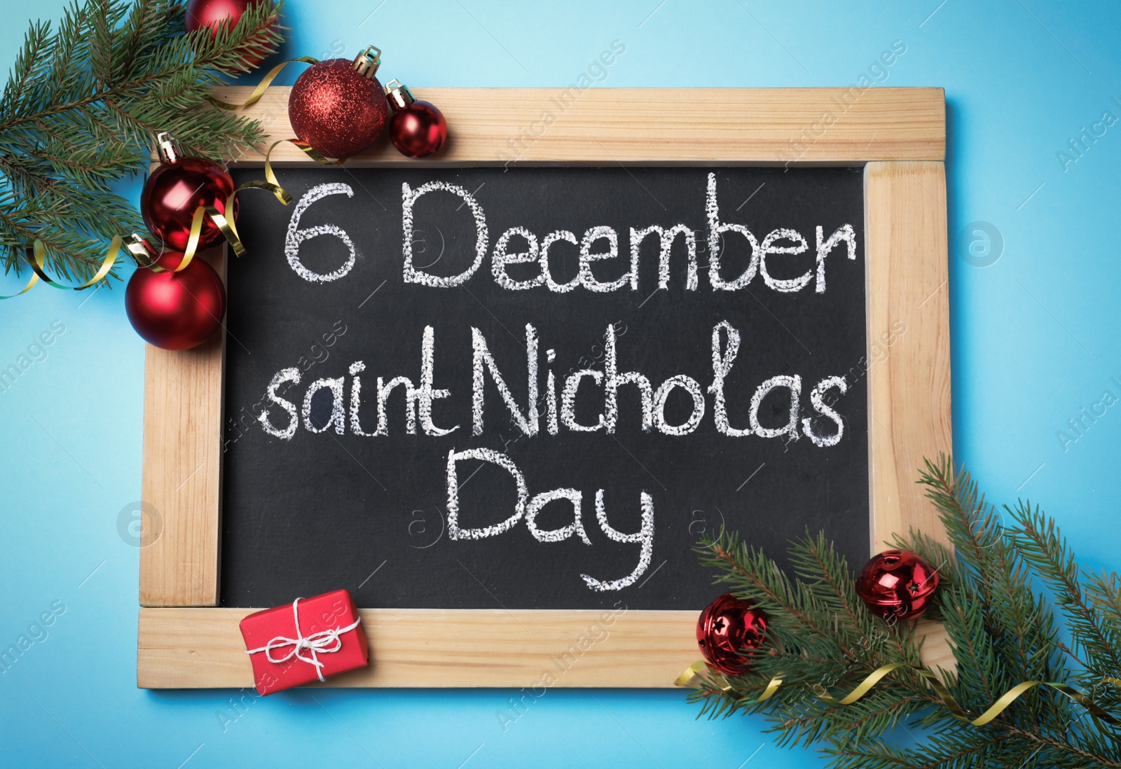 Photo of Small chalkboard with text 6 December Saint Nicholas Day and festive decor on light blue background, flat lay