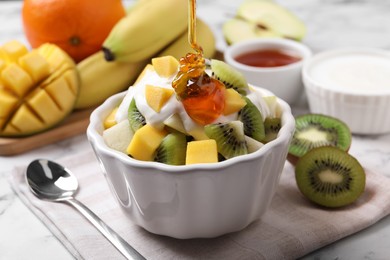 Photo of Pouring honey onto delicious fruit salad in bowl on table