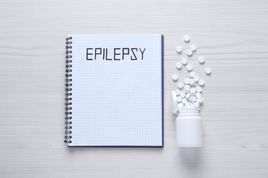 Photo of Notebook with word Epilepsy and pills on white wooden table, flat lay