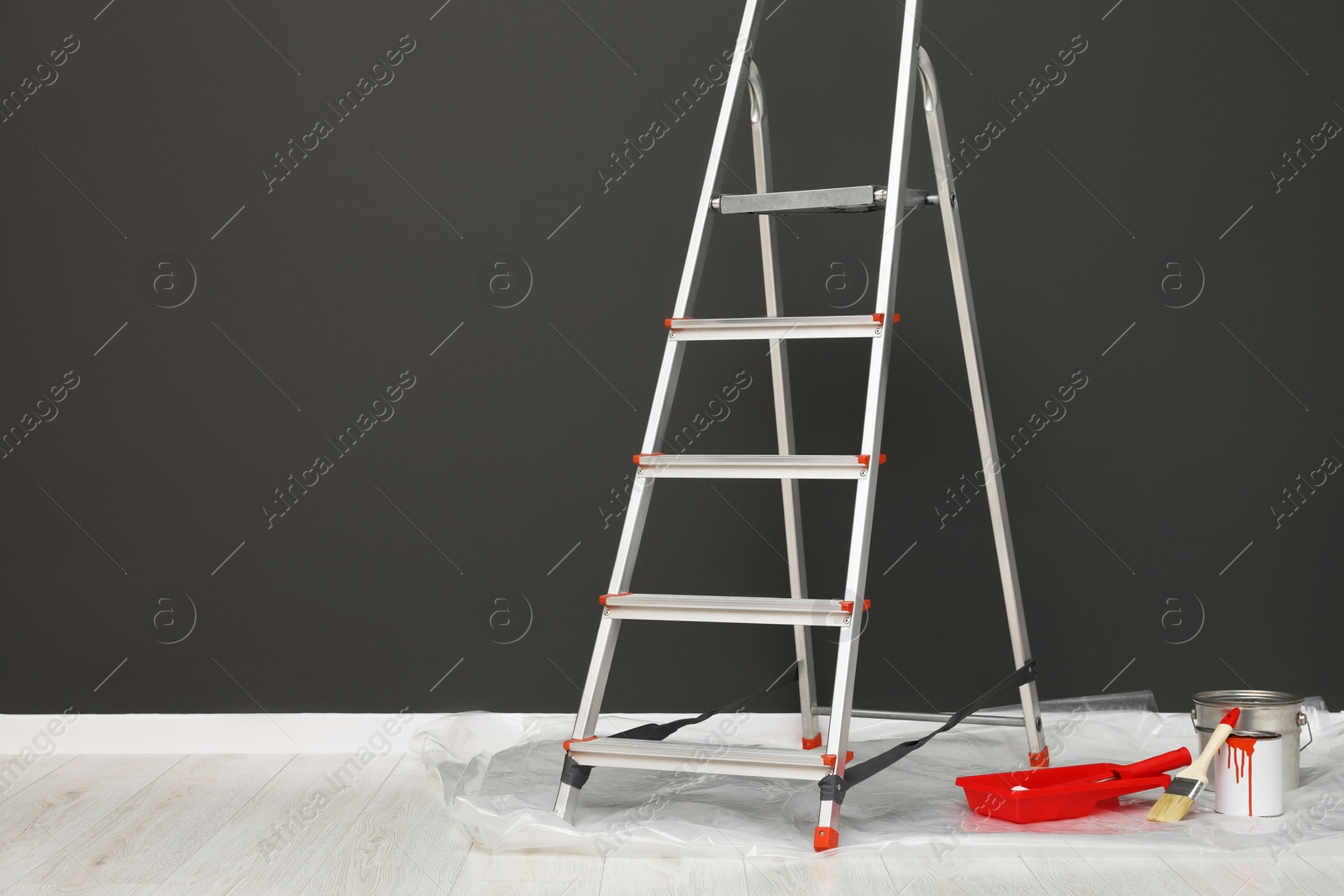 Photo of Metallic folding ladder and painting tools near gray wall indoors, space for text
