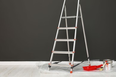 Photo of Metallic folding ladder and painting tools near gray wall indoors, space for text