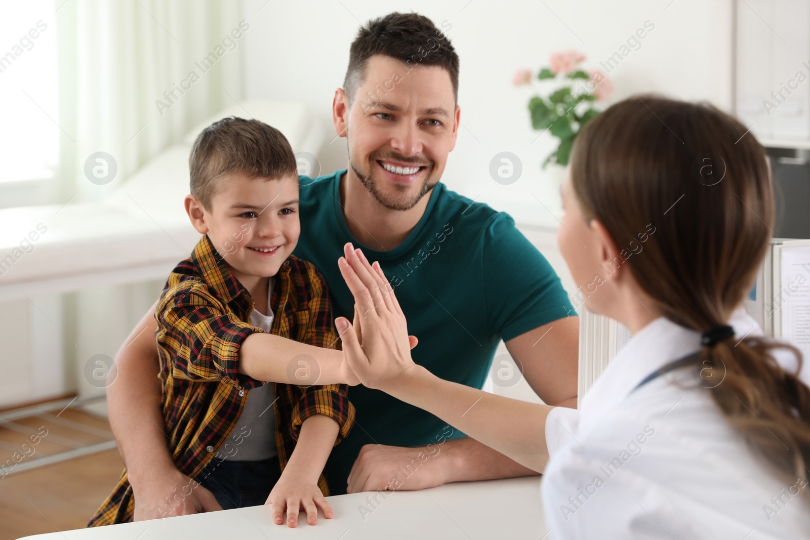 Photo of Father and son visiting pediatrician. Doctor working with little patient in hospital