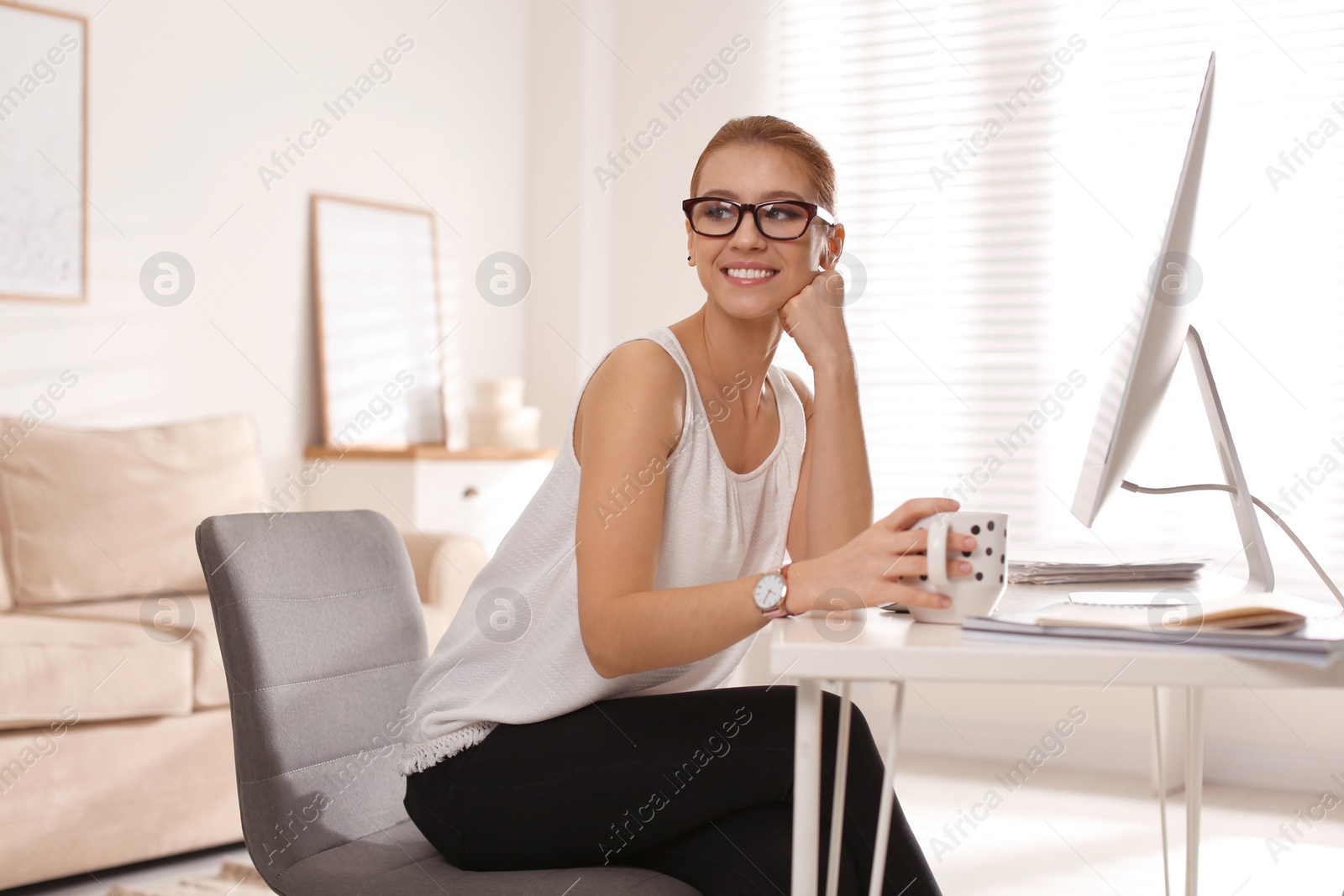 Photo of Young woman with cup of drink relaxing at table in office during break