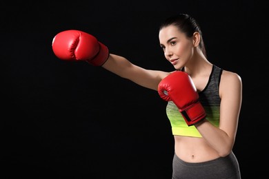 Photo of Beautiful woman in boxing gloves training on black background