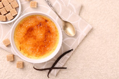 Photo of Delicious creme brulee in bowl, vanilla pods, sugar cubes and spoon on light textured table, top view. Space for text