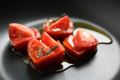 Photo of Melting ice cubes with tomatoes, oil and rosemary on frying pan, closeup