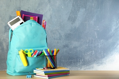 Bright backpack with school stationery on brown wooden table against blue background, space for text