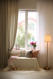 Photo of Comfortable place for rest with cushions and peony flowers near window indoors