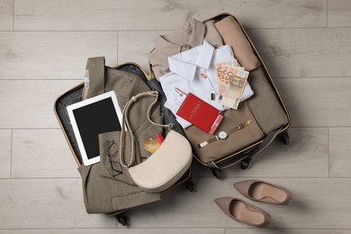 Folded clothes with accessories in open suitcase and shoes on wooden floor, flat lay. Business trip planning