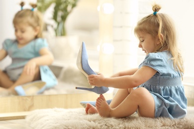 Photo of Cute little girl trying on big high heeled shoes at home