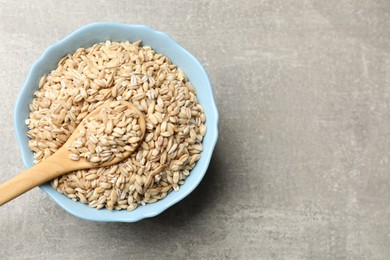 Dry pearl barley in bowl and spoon on gray table, top view. Space for text