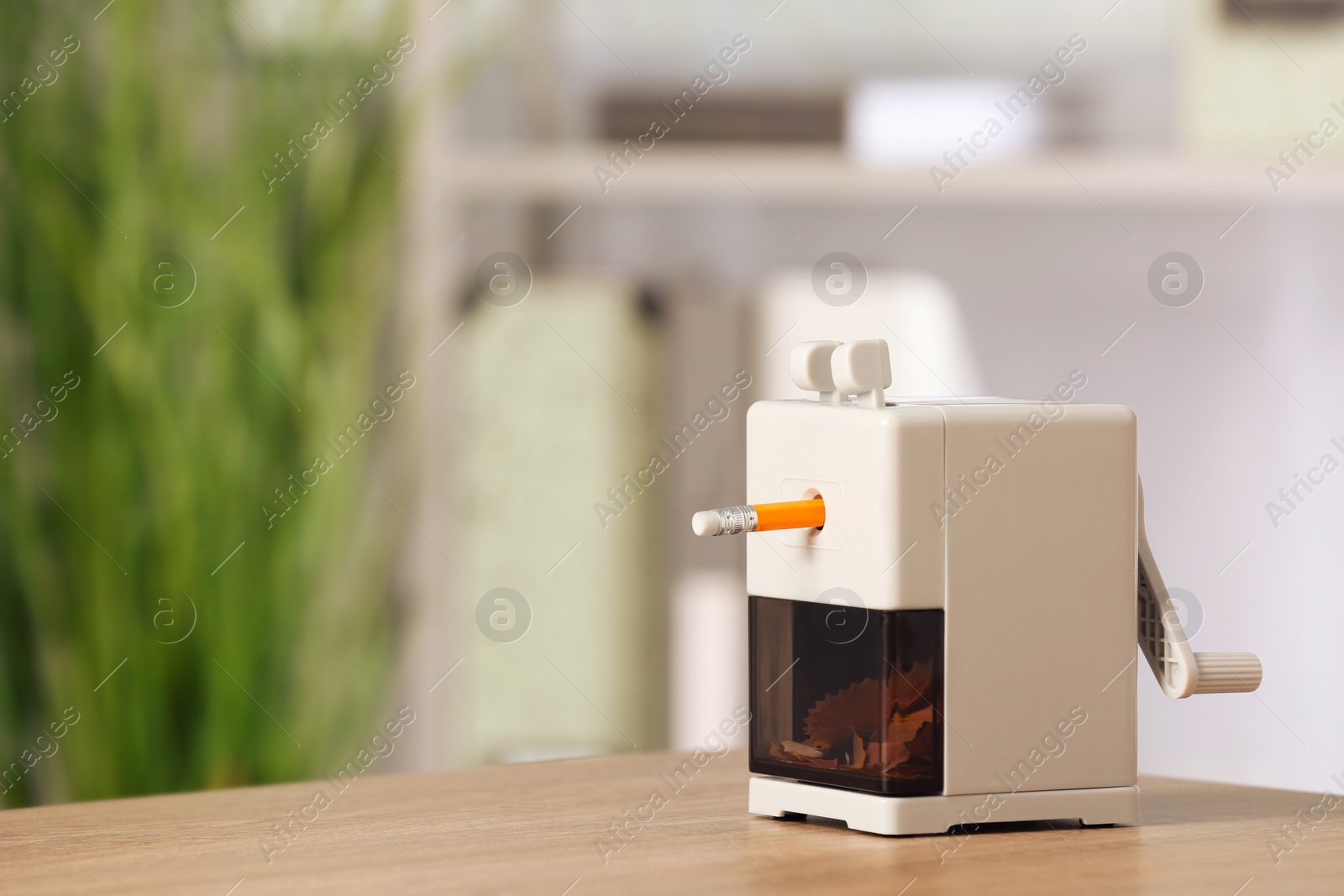 Photo of Mechanical sharpener with pencil on wooden table indoors. Space for text