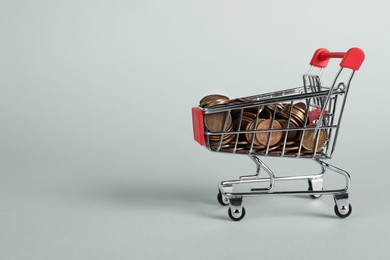 Photo of Small metal shopping cart with coins on light background, space for text