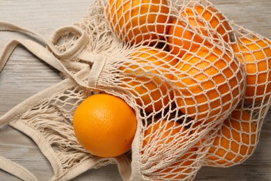 Many ripe juicy oranges with net bag on wooden table, closeup