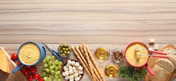 Photo of Flat lay composition with pots of cheese fondue and products on wooden table, space for text