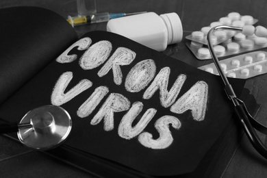 Notepad with words CORONA VIRUS, stethoscope and medicines on grey stone background, closeup