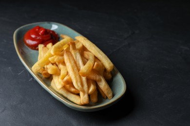 Plate of tasty french fries served with ketchup on black table