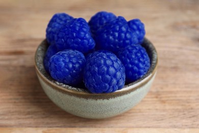 Image of Many fresh blue raspberries in bowl on wooden table, closeup