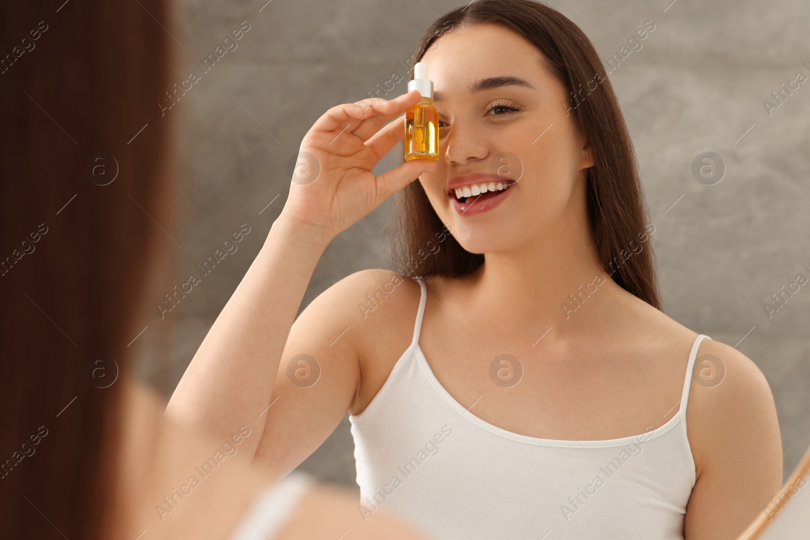 Photo of Happy young woman with essential oil near mirror