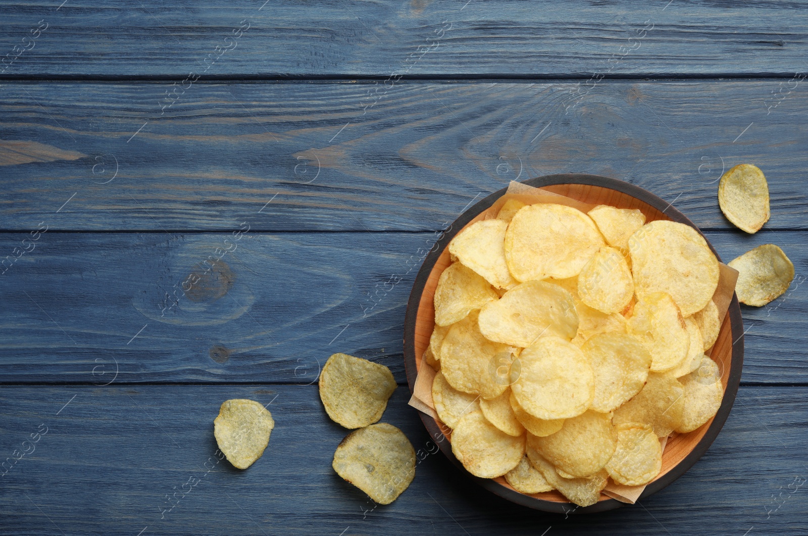 Photo of Bowl and potato chips on wooden table, top view. Space for text