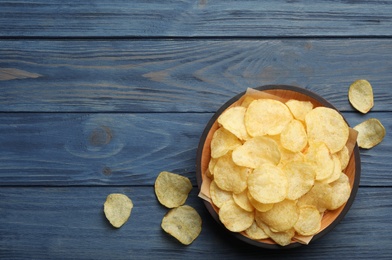 Bowl and potato chips on wooden table, top view. Space for text