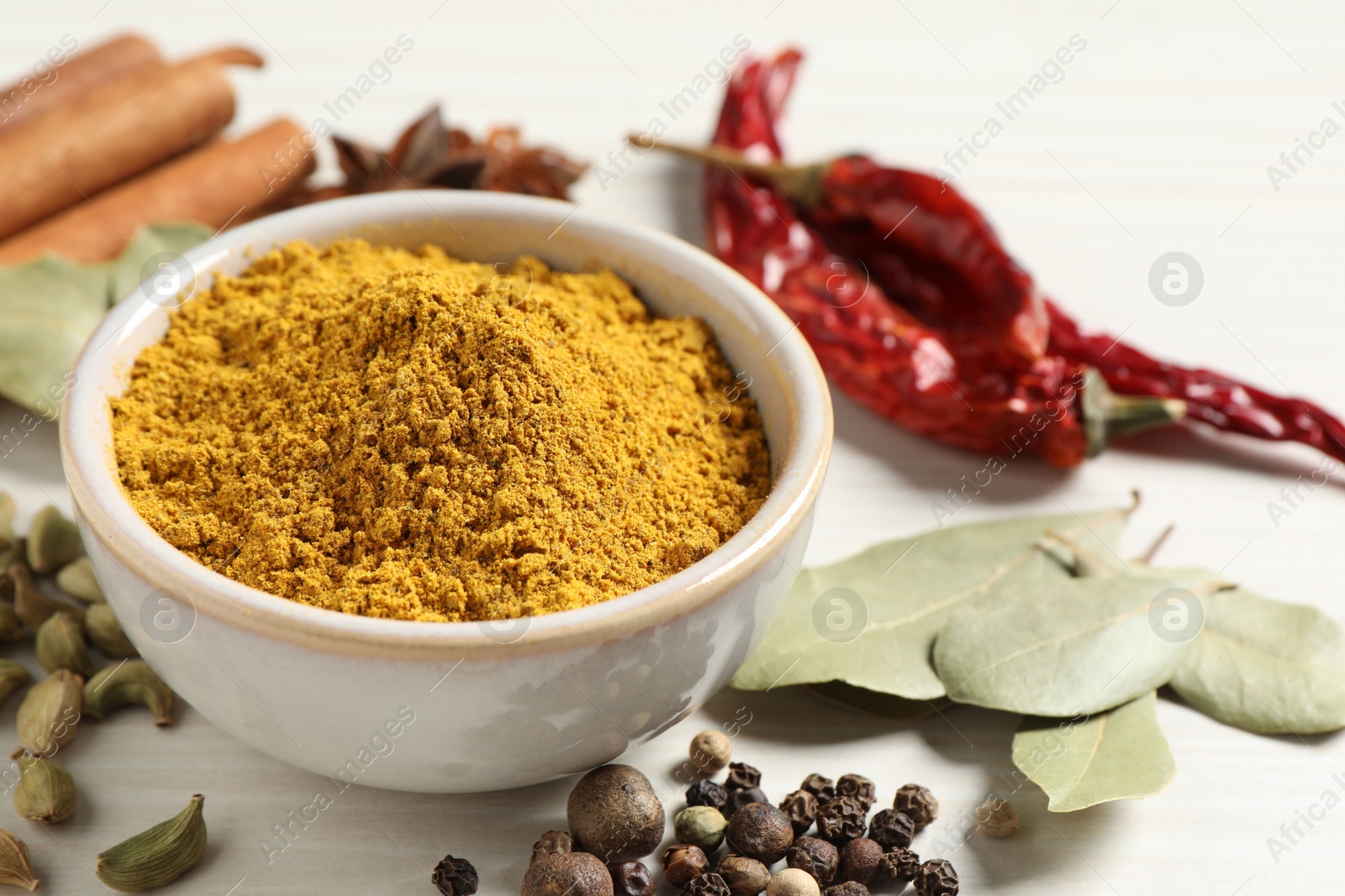 Photo of Curry powder in bowl and other spices on white wooden table, closeup