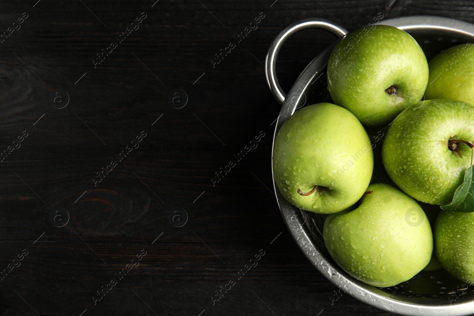 Photo of Colander of fresh ripe green apples on black wooden table, top view. Space for text