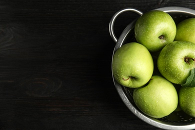 Photo of Colander of fresh ripe green apples on black wooden table, top view. Space for text