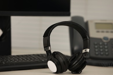 Photo of Modern headphones, desktop telephone and computer on table indoors
