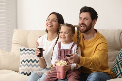 Happy family watching TV with popcorn on sofa indoors, space for text