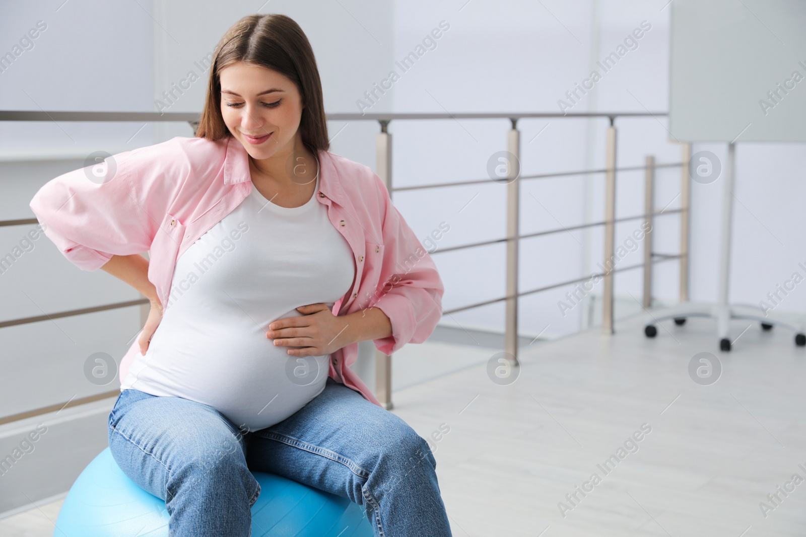 Photo of Pregnant woman sitting on fitball indoors. Space for text