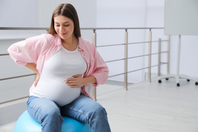 Photo of Pregnant woman sitting on fitball indoors. Space for text