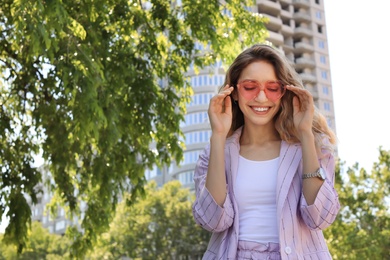 Photo of Portrait of happy young woman with heart shaped glasses in city on sunny day. Space for text