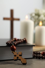 Bible, rosary beads, wooden cross and church candles on grey table, closeup