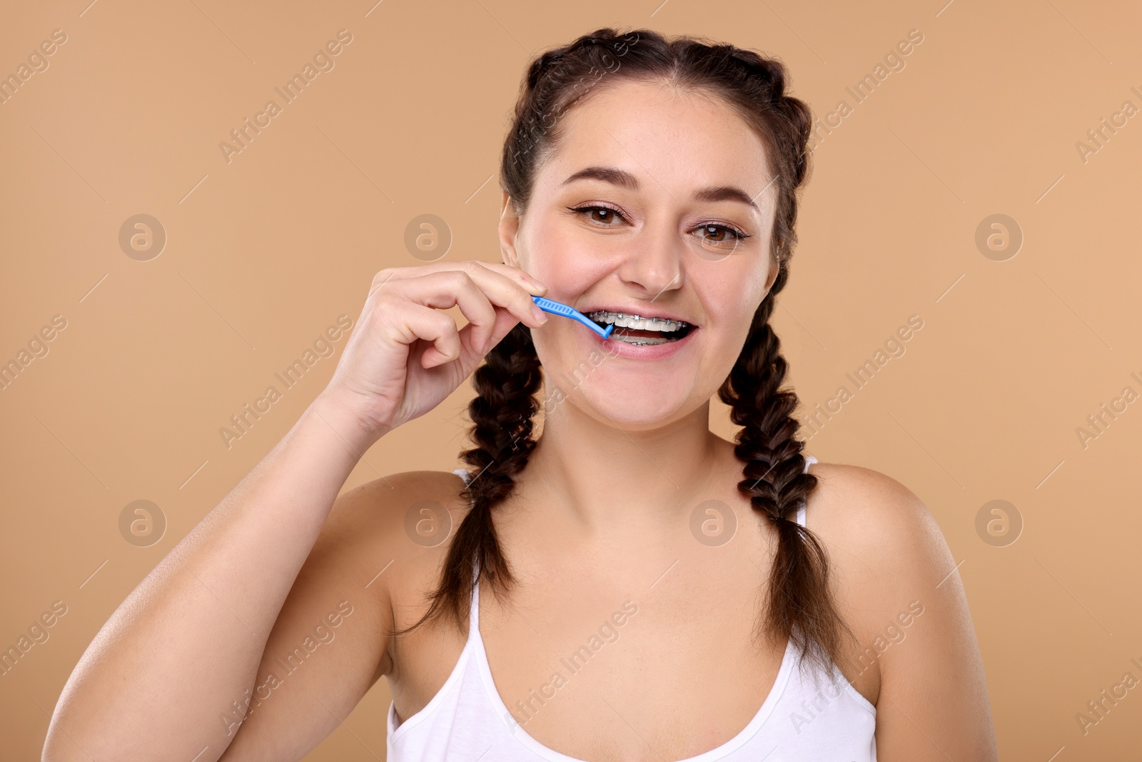 Photo of Smiling woman with dental braces cleaning teeth using interdental brush on beige background