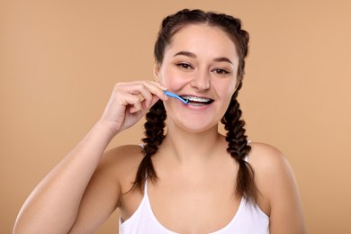 Photo of Smiling woman with dental braces cleaning teeth using interdental brush on beige background